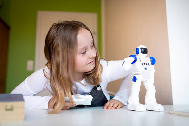 pretty young schoolgirl sitting on her desk in room at home playing with small robot stock photo