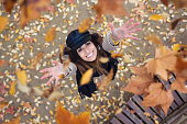 Shot of pretty young woman looking to the sky with arms raised as leaves fall from the trees in the park in autumn.
