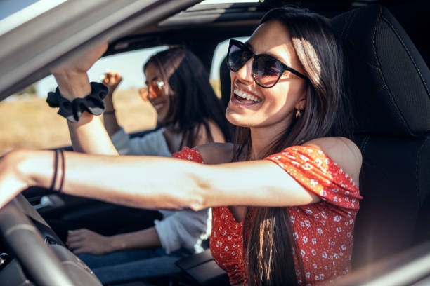 Pretty young women singing while driving a car on road trip on beautiful summer day. stock photo
