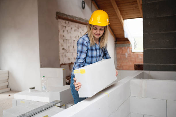 pretty young worker woman with yellow safety helmet works on construction site and puts up a wall stock photo