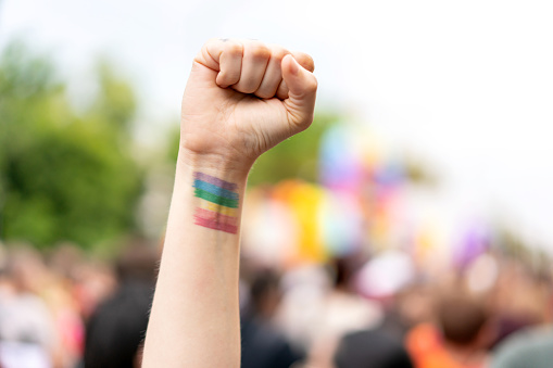 A raised hand in the air forming a fist with the pride flag during a parade