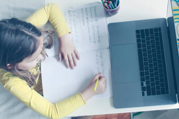 Primary school girl doing homework at home at the computer on the online platform. stock photo