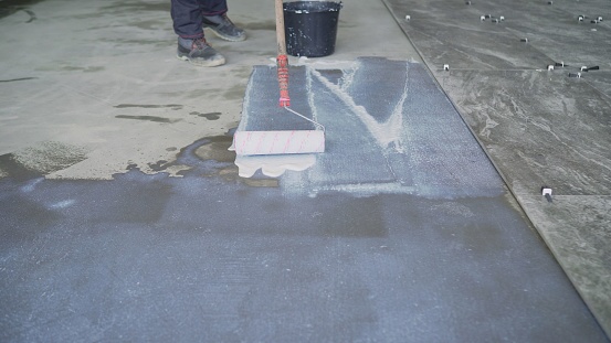 Large scale application of a primer to concrete floors. Priming the floor with a roller. Priming Concrete floor before laying tiles on it, the final preparatory stage for strengthening the surface.