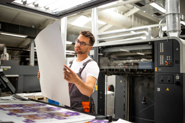 print shop worker checking quality of imprint and controlling printing process. - drukken stockfoto's en -beelden