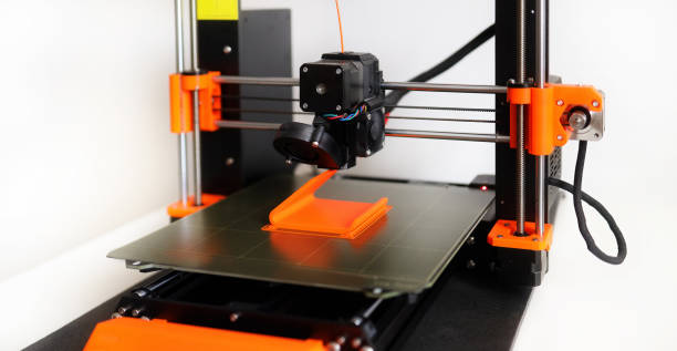 3D Printer in operation with orange filament on a white background stock photo