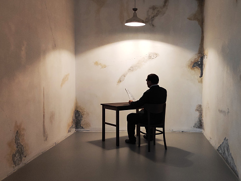 Prisoner silhouette sitting under spotlight in interrogation room