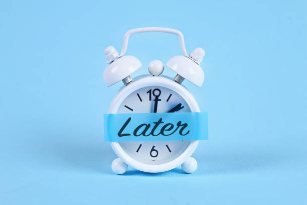 Procrastination, delay, urgency concept. White alarm clock with a sticky note with text later. Procrastination, delay and urgency concept. White alarm clock with a sticky note with text later. postponed stock pictures, royalty-free photos & images