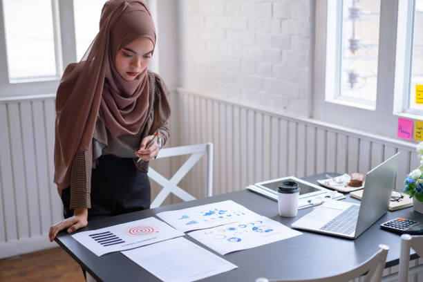 professionele arabische zakenvrouw brown hijab staande en controle van de financiële investeringsproject graph chart rapport. indoor - business malaysia stockfoto's en -beelden