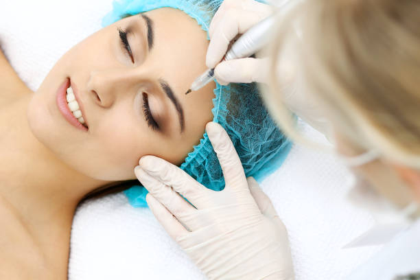 Professional beautician doing eyebrow tattoo at woman face. Permanent brow makeup in beauty salon, closeup.  Cosmetology treatmen stock photo