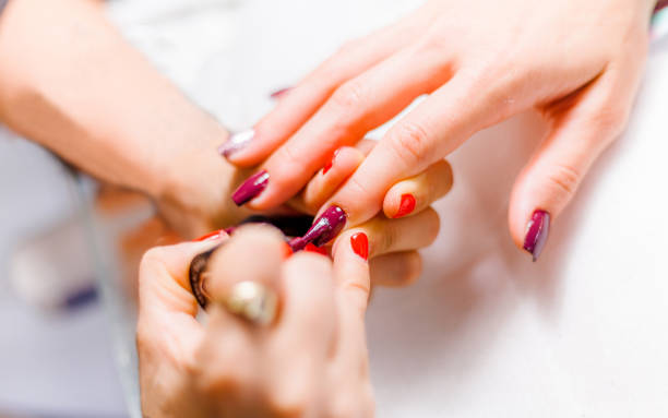 Professional beautician paiting the nails of a client Professional beautician is paiting the nails of a client wiht red and purple painting fingernails stock pictures, royalty-free photos & images