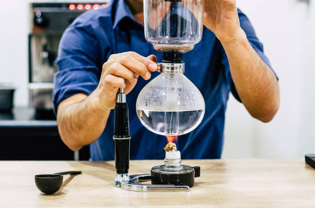 Professional coffee maker - Barista using coffee siphon brewing hot espresso at coffee shop. Professional coffee maker - Barista using coffee siphon brewing hot espresso at coffee shop siphon stock pictures, royalty-free photos & images