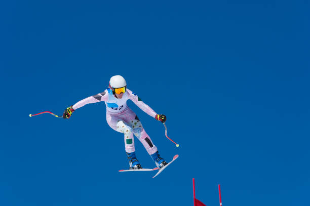 Professional female skier jumping on the red gate during downhill race stock photo