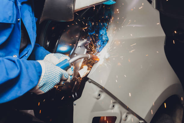 professional repairman worker in automotive industry welding metal body car with sparks. stock photo