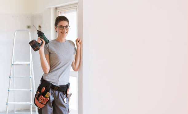 Professional repairwoman posing and holding a drill Professional repairwoman with tool belt doing a home renovation, she is posing and holding a drill restoring stock pictures, royalty-free photos & images