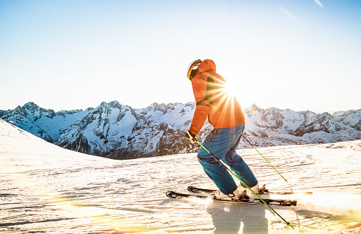 Professional skier athlete skiing at sunset on top of french alps ski resort - Winter vacation and sport concept with adventure guy on mountain top riding down the slope - Warm bright sunshine filter