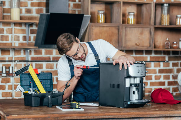 professional young worker in eyeglasses and protective workwear fixing coffee machine professional young worker in eyeglasses and protective workwear fixing coffee machine coffee maker stock pictures, royalty-free photos & images