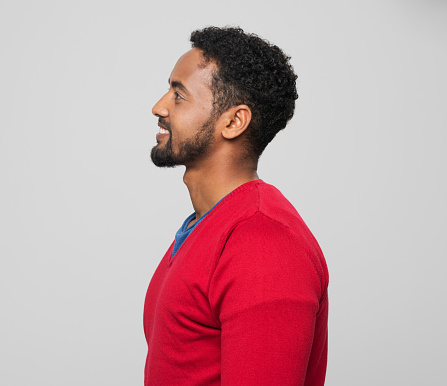 Side view of smiling young man in red sweater standing against grey background.