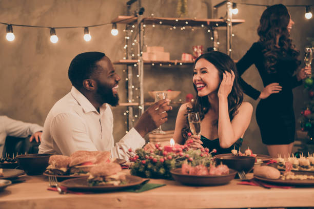 Profile side photo of cheerful couple of mixed-race man and chinese woman give toast hold champagne speak enjoy christmas, party x-mas night in house with table full of new year dinner feat indoors  holidays and celebrations stock pictures, royalty-free photos & images