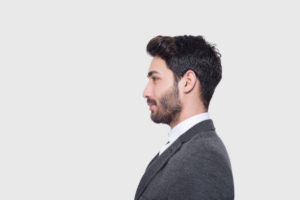 Profile view of young businessman in suit looking away over gray background stock photo