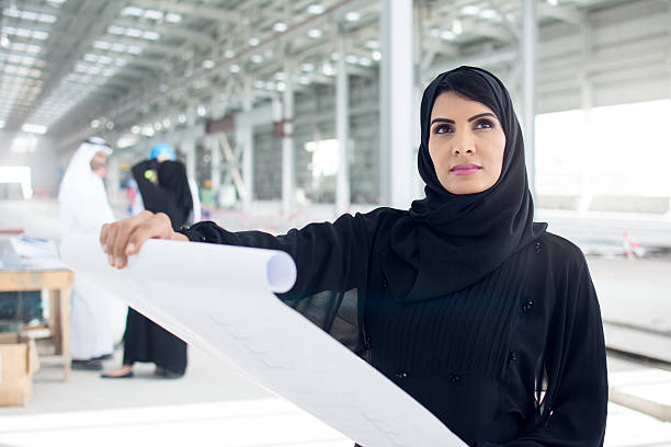Project is coming together Arabic businesswoman is looking at blueprints and her construction project. abaya clothing stock pictures, royalty-free photos & images