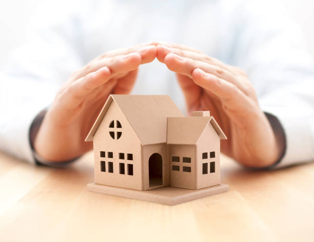 Property insurance. House miniature covered by hands. stock photo
