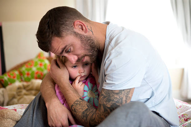Protective Father A father comforts his upset little girl, he hugs her tightly. The little girl looks upset and tired. mourner stock pictures, royalty-free photos & images