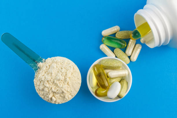 Protein powder in measuring plastic spoon and vitamin complex, omega 3, glucosamine capsules, supplements on blue background, sports nutrition, top view Protein powder in measuring plastic spoon and vitamin complex, omega 3, glucosamine capsules, supplements on blue background, sports nutrition, top view. glucosamine stock pictures, royalty-free photos & images