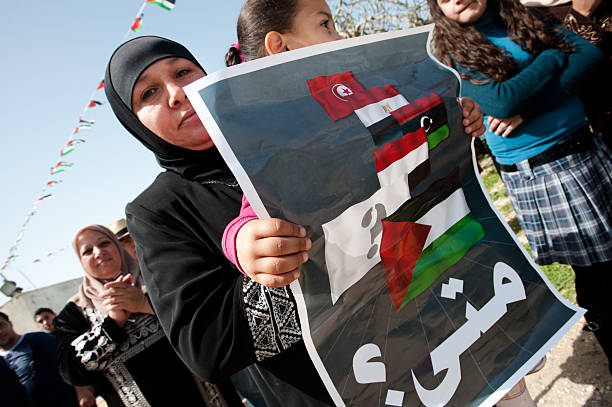Protest in Palestine "Nabi Samuel, Occupied Palestinian Territories - April 1, 2011: A Palestinian mother and daughter hold a sign with the flags of Tunisia, Egypt, Libya, Yemen, and Palestine with the question in Arabic: &quot;When&quot; at an olive planting event in observance of Land Day 2011." tunisian girls stock pictures, royalty-free photos & images