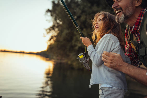Proud grandfather helping out his granddaughter with fishing stock photo