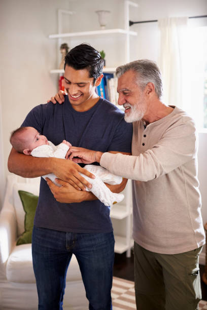 proud senior hispanic man standing with his adult son holding his four month old boy, vertical - grandparents vertical imagens e fotografias de stock