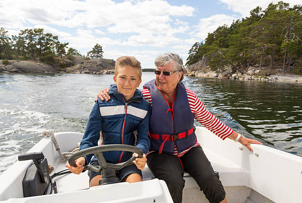 Proud young captain running small motor boat with grandmother. stock photo