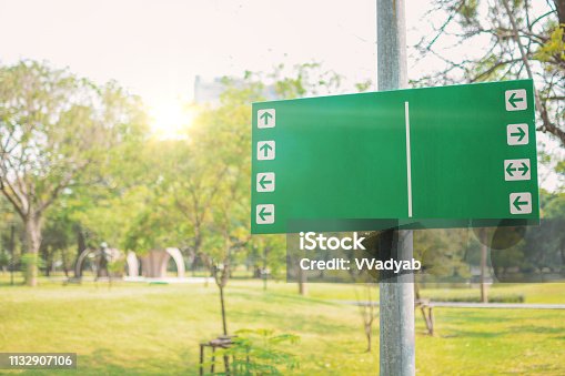 istock Public park with empty green trailhead sign showing  multiple trails and nature landscape background in morning.Green sign in park with flare light 1132907106