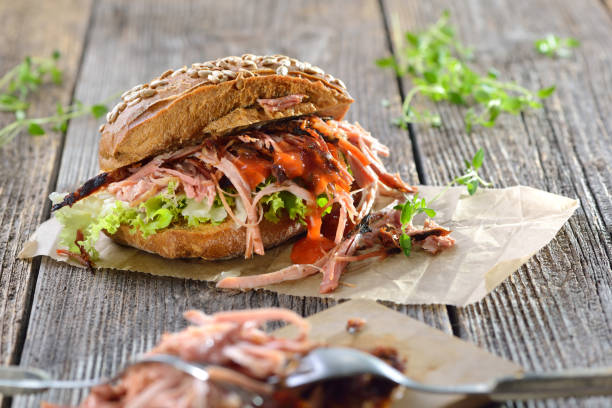 Pulled pork sandwich Street food: Barbecue pulled pork wholemeal sandwich with coleslaw, hot BBQ sauce served on brown wrapping paper on a wooden background burger wrapped in paper stock pictures, royalty-free photos & images
