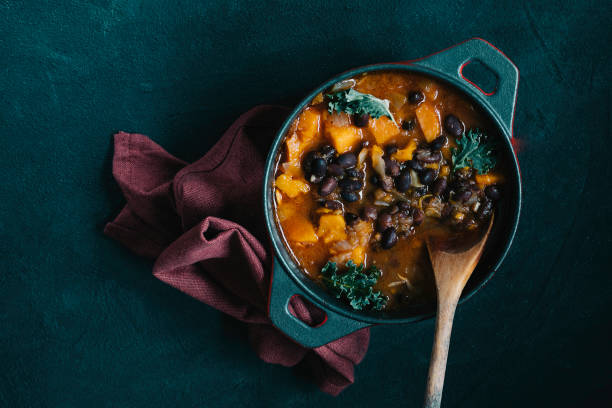 pumpkin and black beans  chili an iron casserole with beans with a garnet napkin on a black background casserole dish stock pictures, royalty-free photos & images