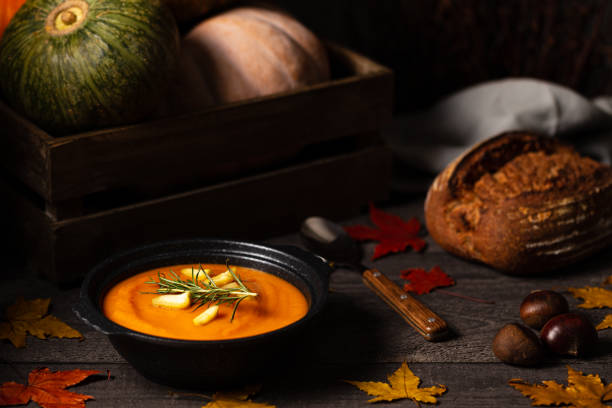 Pumpkin and chestnut soup with rosemary twig aside pumpkins in a crate and chestnuts on a vintage dark wood background spread with maple leaves. stock photo