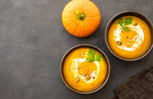 Pumpkin soup in a bowl with fresh pumpkins, garlic and parsley herbs on a black background. Autumn concept. stock photo