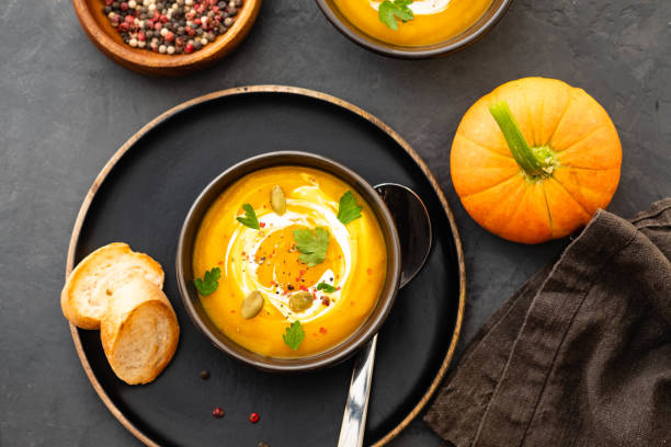 Pumpkin soup in a bowl with fresh pumpkins, garlic and parsley herbs on a black background. Autumn concept. stock photo