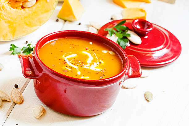 Pumpkin soup in a red bowl Pumpkin soup in a red bowl on white wooden background, selective focus thanksgiving diner stock pictures, royalty-free photos & images
