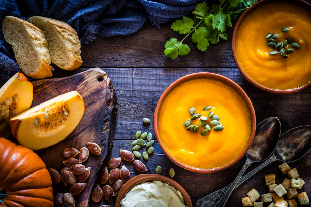 Pumpkin soup with ingredients on rustic wooden table Two brown bowls filled with homemade pumpkin soup surrounded by ingredients for preparing soup shot from above on rustic wooden table. Predominant colors are orange and brown. Low key DSRL studio photo taken with Canon EOS 5D Mk II and Canon EF 100mm f/2.8L Macro IS USM. thanksgiving food stock pictures, royalty-free photos & images