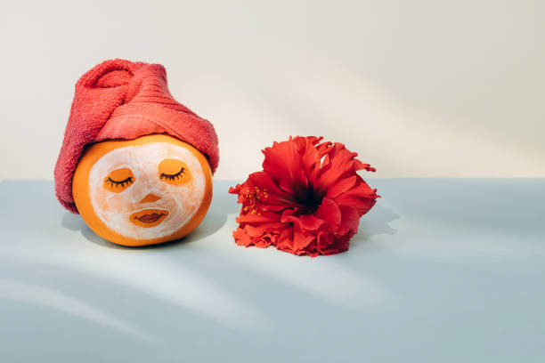 Pumpkin with facial mask, towel and flower on pastel background with shadow from palm leaves stock photo