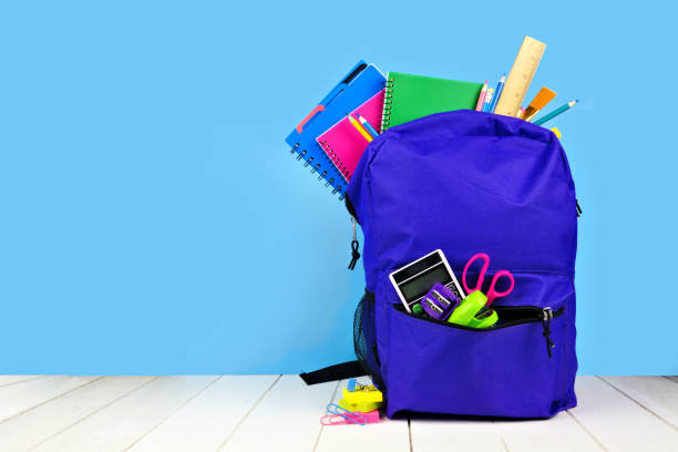 purple rugzak vol met schoolbenodigdheden tegen een blauwe achtergrond. terug naar school. - backpack stockfoto's en -beelden