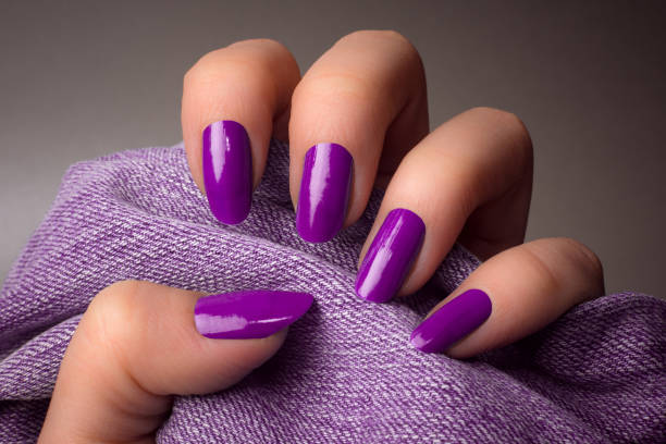purple nails manicure The female hand with purple nails is holding purple denim textile on gray background. Manicure concept. artificial nail stock pictures, royalty-free photos & images