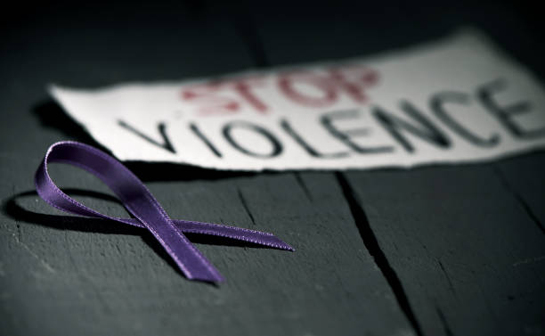 purple ribbon against the violence against women a purple ribbon for the awareness about the unacceptability of the violence against women and the text stop violence on a piece of paper, on a dark gray rustic wooden surface domestic violence stock pictures, royalty-free photos & images