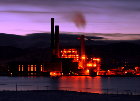A view of a power plant lit with sodium lights.  The setting sun has turned the sky a pale purple.