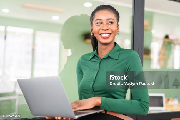Purposeful African-American businesswoman in smart casual wear stand in modern coworking space and holding laptop