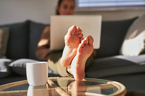 Shot of a young woman using a laptop on the sofa at home with coffee in the foreground