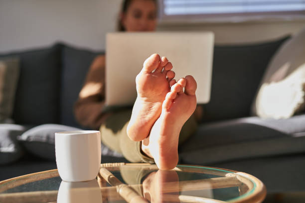Put your feet up, it's time to relax Shot of a young woman using a laptop on the sofa at home with coffee in the foreground barefoot stock pictures, royalty-free photos & images