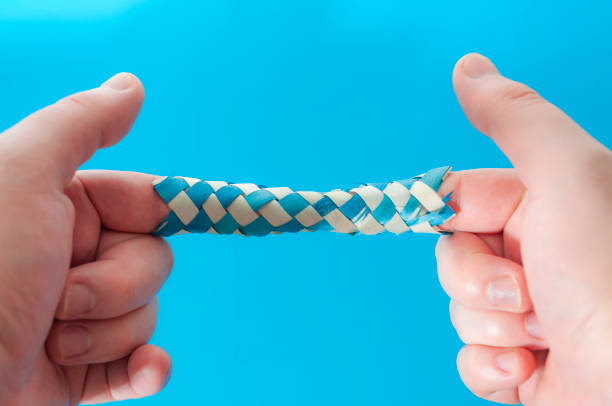 Puzzle game and logic games concept with hands playing with a chinese finger trap, a toy that the more you pull the tighter it gets stuck and you need to push to escape isolated on blue background stock photo
