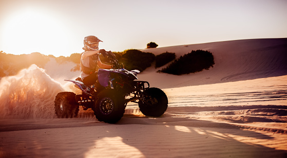 Professional quad bike racer driving on sand dunes in protective gear