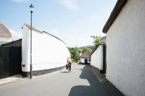 Dunsford, England - July 23, 2013: Narrow English rural village lane with high white walls and cyclist taking advantage of the quiant towns as he passes through.